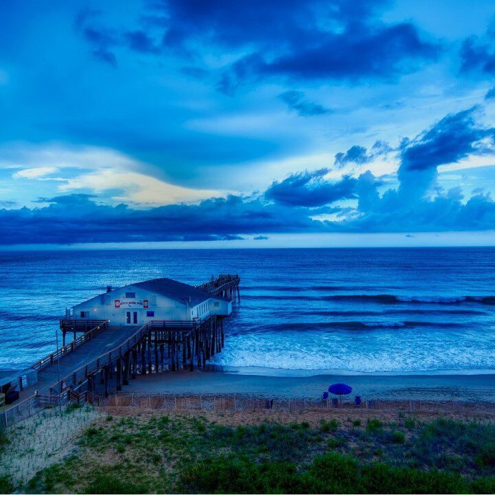 A pier on the beach with waves crashing in front of it.