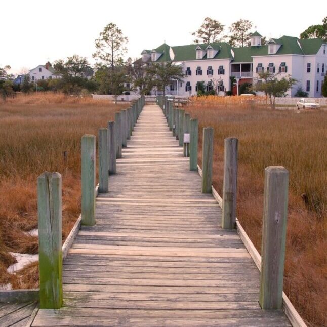 A wooden walkway leading to a large house.