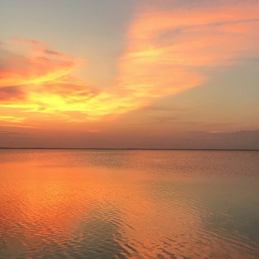 A sunset over the ocean with orange clouds in the sky.